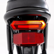 Close-up rear view of a black motorized scooter or moped showing two red taillights illuminated against a white background.