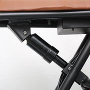 Close-up detail of a black metal support frame and hydraulic or mechanical cylinder mechanism, with part of a brown padded surface visible at the top against a light gray background.
