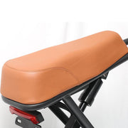 A close-up of a tan or light brown faux leather motorcycle or bicycle seat cushion mounted on a black frame, with a small red taillight visible below.