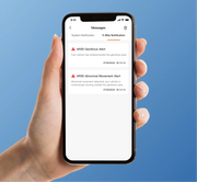 A hand holding a black smartphone against a solid blue background. The phone screen displays a messages app with two e-commerce geofence alert notifications.