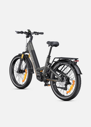 A dark gray electric bicycle with black components, bright orange accents on the wheel spokes and fork, and a rear cargo rack, shown on a light gray background.