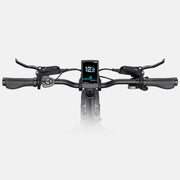 A close-up, front-facing view of a black electric bicycle handlebar setup, featuring a central digital display screen showing speed and battery status, with brake levers on both sides.