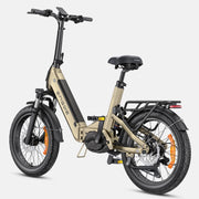 A compact electric bicycle with a tan and black frame, black tires, and orange wheel reflectors, shown from a three-quarters front angle on a light gray background.